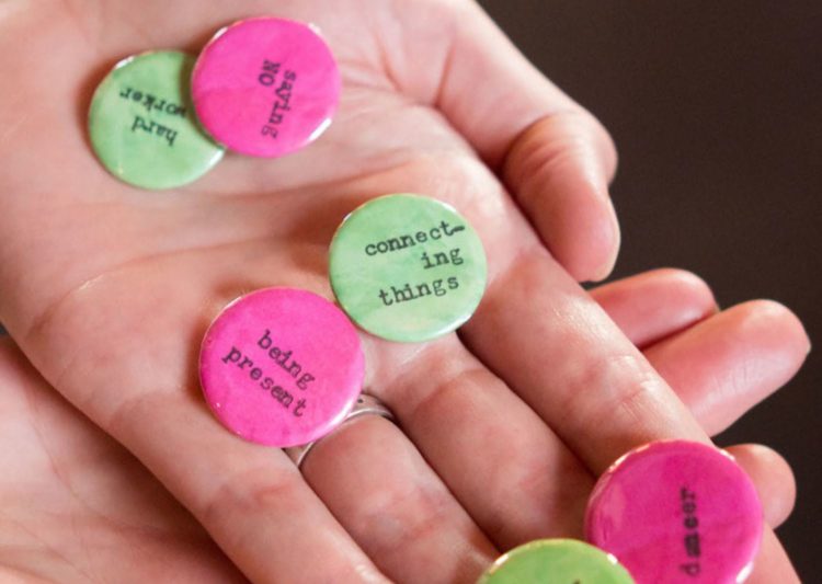 A light-skinned hands holds a handful of buttons with affirmations like, "Being present" and "Connecting things."