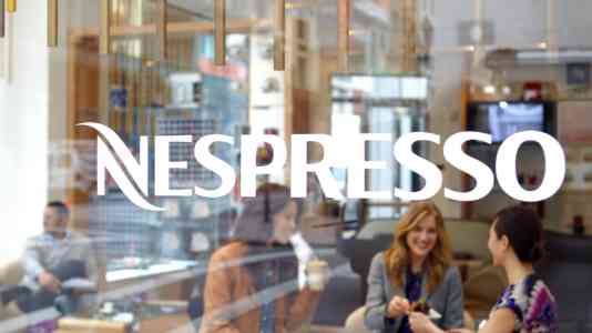 A group of women is seated inside a Nespresso coffee shop. The white Nespresso logo is superimposed on the image.